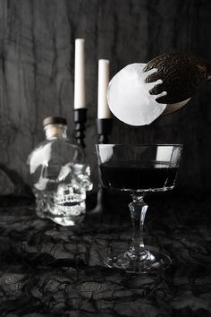 a glass filled with black liquid next to two empty bottles and candles on a table