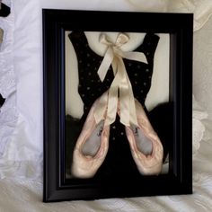 two pairs of ballet shoes are framed in a black and white frame on a bed