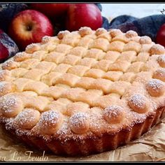 an apple pie with powdered sugar on top and some apples in the back ground