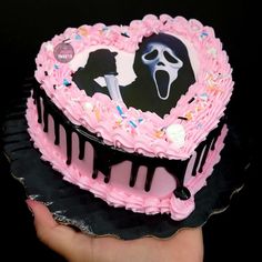 a heart shaped cake decorated with pink icing and sprinkles, on top of a black plate