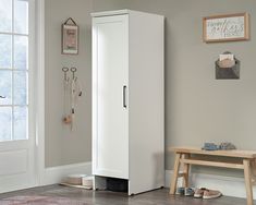 a tall white cabinet sitting next to a wooden bench in a room with a rug on the floor