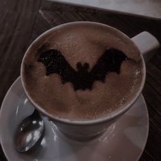 a cup of hot chocolate with a bat drawn on the foam and spoon in it