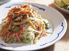 a white plate topped with noodles and veggies next to a bowl of pickles