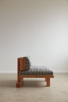 a wooden bench with plaid fabric on it in front of a white wall and floor