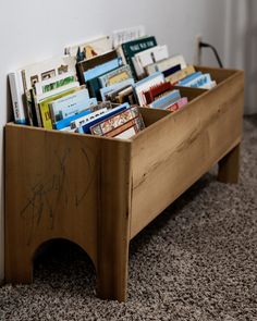 a wooden box filled with books sitting on top of a carpeted floor next to a wall