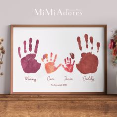 three handprints are displayed in front of a vase with flowers on the shelf