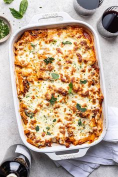 a casserole dish with meat and cheese in it next to two glasses of wine