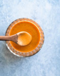 a wooden spoon in a glass cup filled with orange liquid on a light blue surface