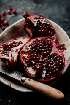 two pomegranates on a plate with a knife and some other food