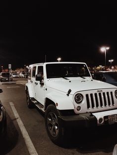 a white jeep is parked in a parking lot at night with other cars around it