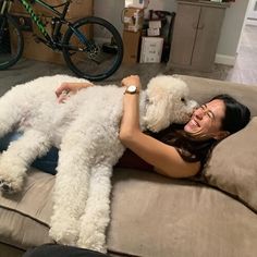 a woman laying on top of a couch holding a white dog