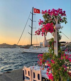 an outdoor dining area overlooking the water with pink flowers on it and a boat in the background