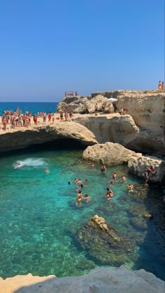 people are swimming in the clear blue water near some rocks and cliffs on a sunny day