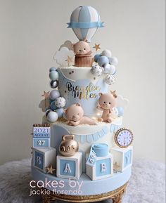 a blue and white baby shower cake with balloons on the top, teddy bears around it