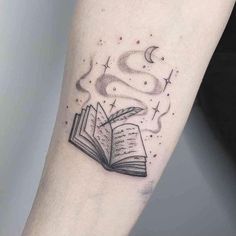 an open book tattoo on the arm with stars and crescents above it, in black ink