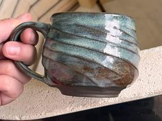 a hand holding a coffee cup that looks like it has been made out of clay