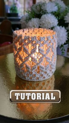 a crocheted candle holder sitting on top of a table next to white flowers