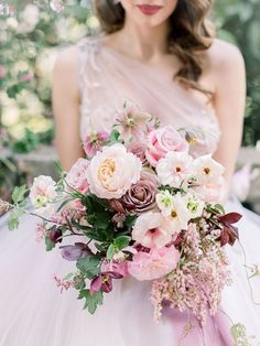 a woman in a wedding dress holding a bouquet of pink and white flowers with greenery