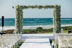 an outdoor ceremony set up with white chairs and greenery on the aisle, overlooking the ocean