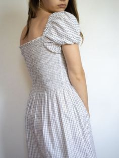 a woman wearing a white and black checkered dress standing in front of a wall