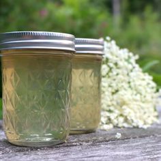 two jars filled with liquid sitting on top of a wooden table next to white flowers