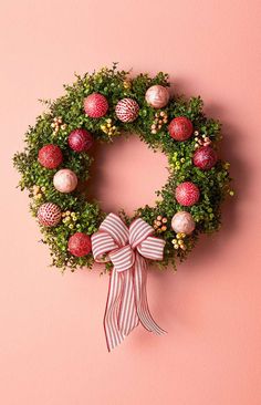 a christmas wreath on a pink wall with red and white ornaments hanging from the front