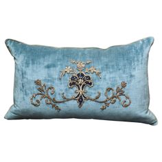 a blue and gold pillow with an ornate design on the front, sitting against a white background