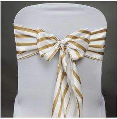 the back of a white chair with gold striped sashes and bow tie on it