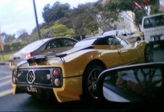 a yellow sports car driving down the street next to a white truck and some trees