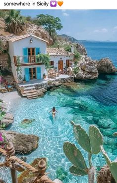 a person swimming in the water next to a house and some cactus plants on the beach