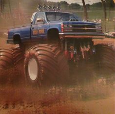 a blue truck with huge tires driving down a dirt road