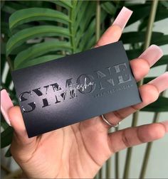 someone holding up a black business card with the words stay strong on it in front of a plant