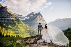 a bride and groom holding hands on top of a mountain