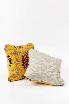 two pillows sitting next to each other on top of a white surface with yellow and red designs