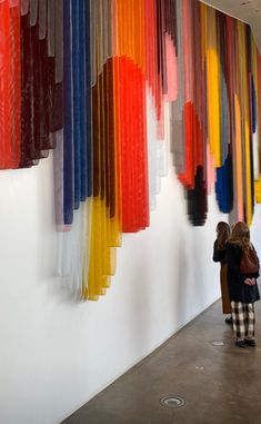 a woman standing next to a wall covered in colorful ribbons