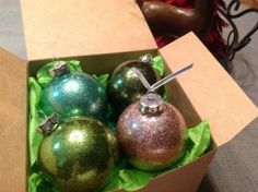 three shiny christmas ornaments in a box on a bed with red and green decorations behind them