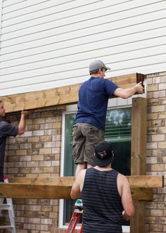 two men are working on the side of a house with wood boards attached to it