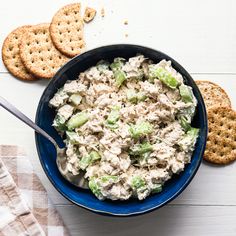 a blue bowl filled with chicken salad next to crackers on top of a white table