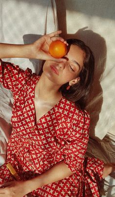 a woman laying in bed holding an orange up to her face