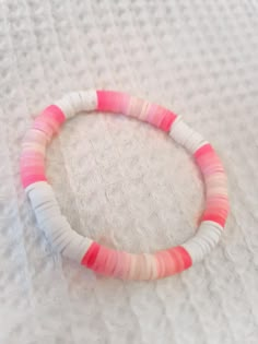 a pink and white beaded bracelet sitting on top of a bed