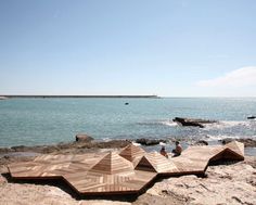 two people are sitting on the rocks by the water and looking out at the ocean