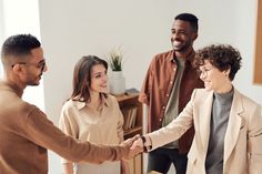 three people are shaking hands in the living room while another person smiles and looks on