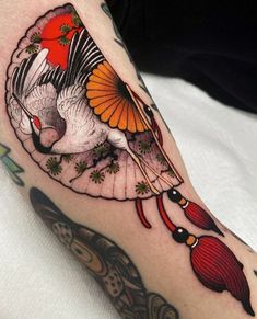 a woman's arm with a bird and fan tattoo on it