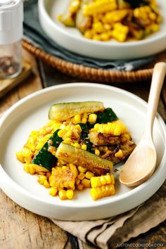 two white plates filled with corn and zucchini on top of a wooden table