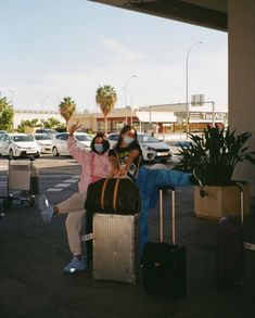 two people sitting on luggage at an airport with masks covering their faces as they pose for the camera