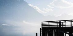 a person is standing on a dock by the water with mountains in the back ground