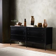 a black dresser with three vases on top of it next to a white rug