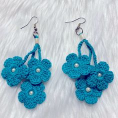 two crocheted flower earrings with pearls hanging from them on a white furnishing