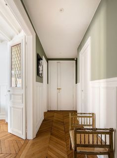 an empty hallway with wooden floors and white doors on either side of the door are two chairs