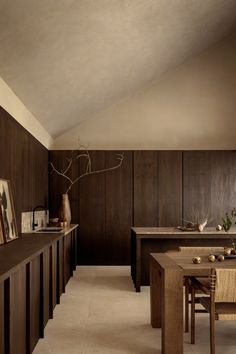 a dining room with wood paneling and wooden table surrounded by chairs, vases and pictures on the wall